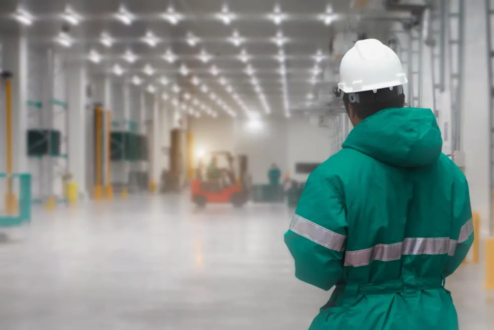 Industrial worker in green safety suit and hard hat in warehouse facility