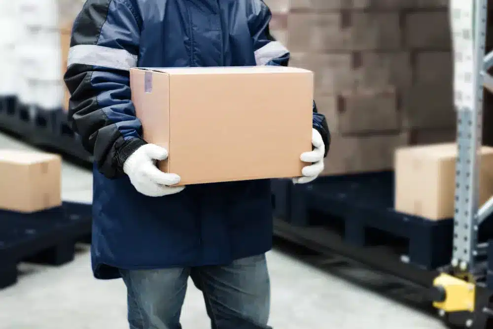 Warehouse worker in blue jacket carrying cardboard box in distribution center