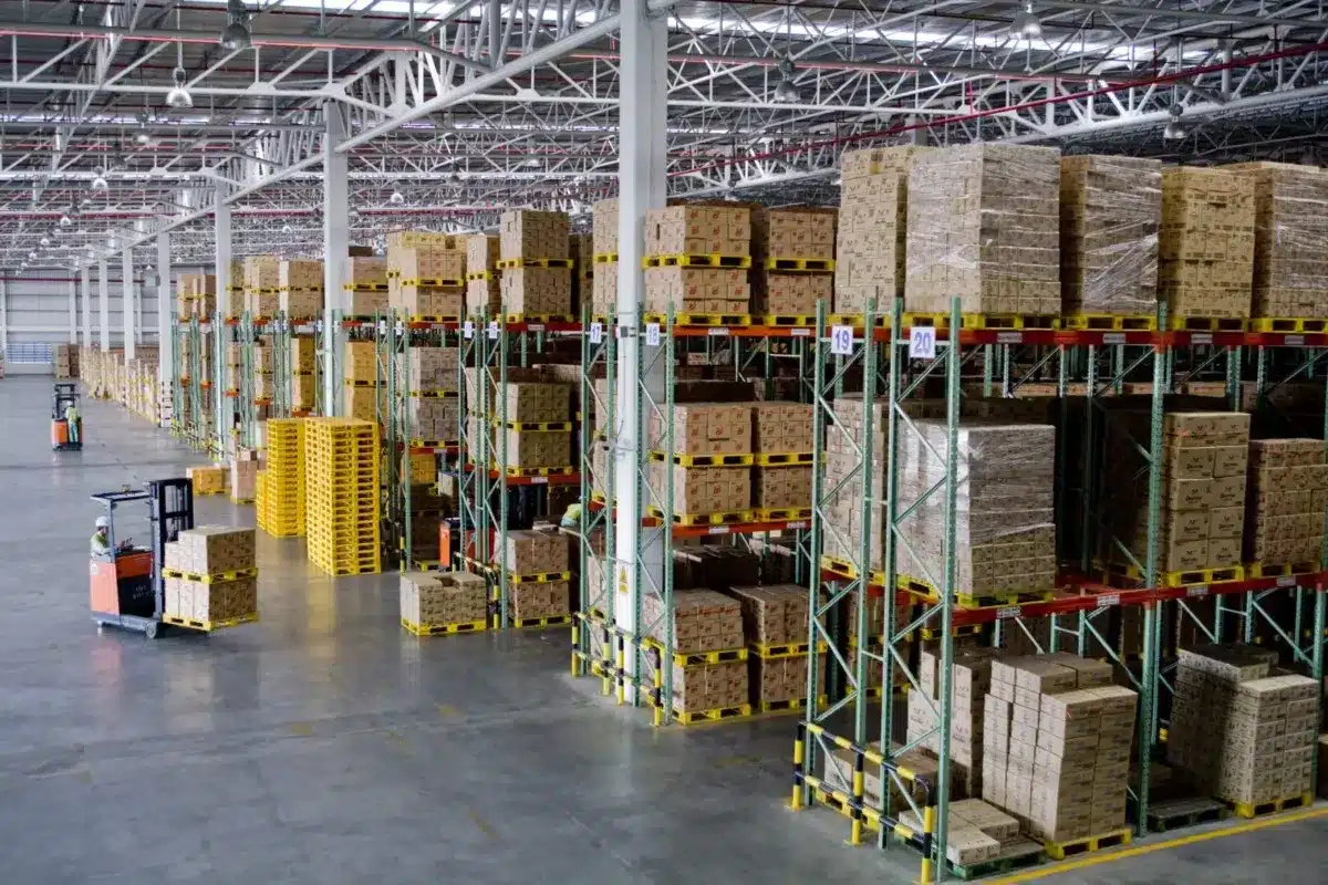 Large warehouse interior with tall storage racks filled with boxed inventory and forklift