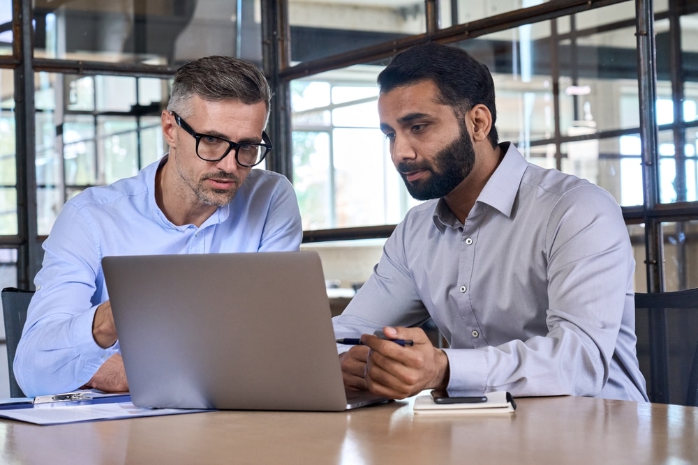 two male professionals discussing asset lifecycle management program at computer