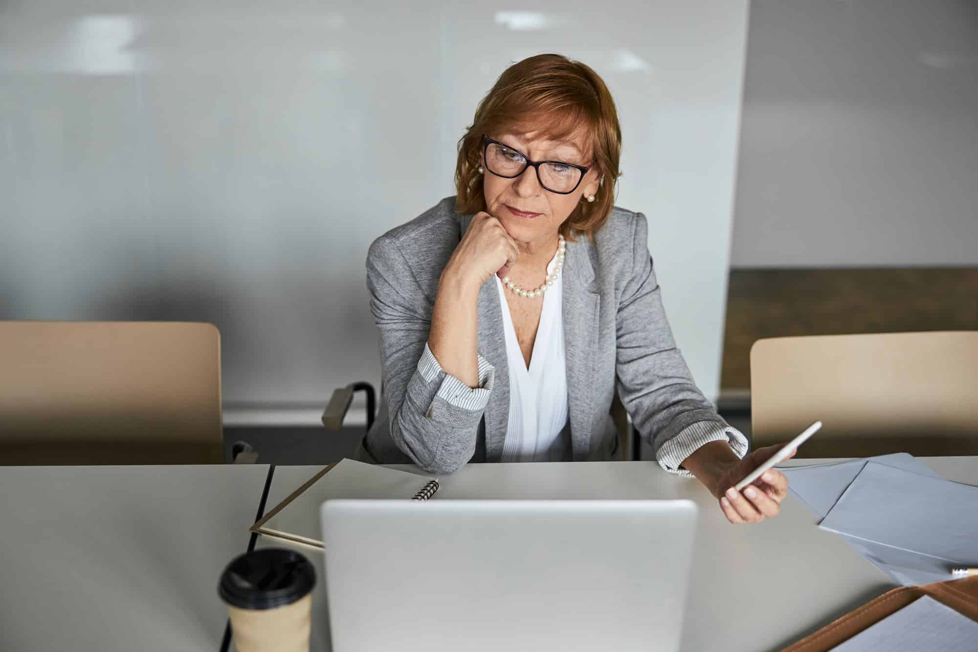 business woman looking at a laptop while holding a phone