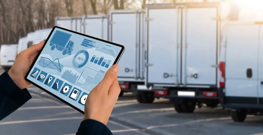 hands holding freight management tablet near truck trailes